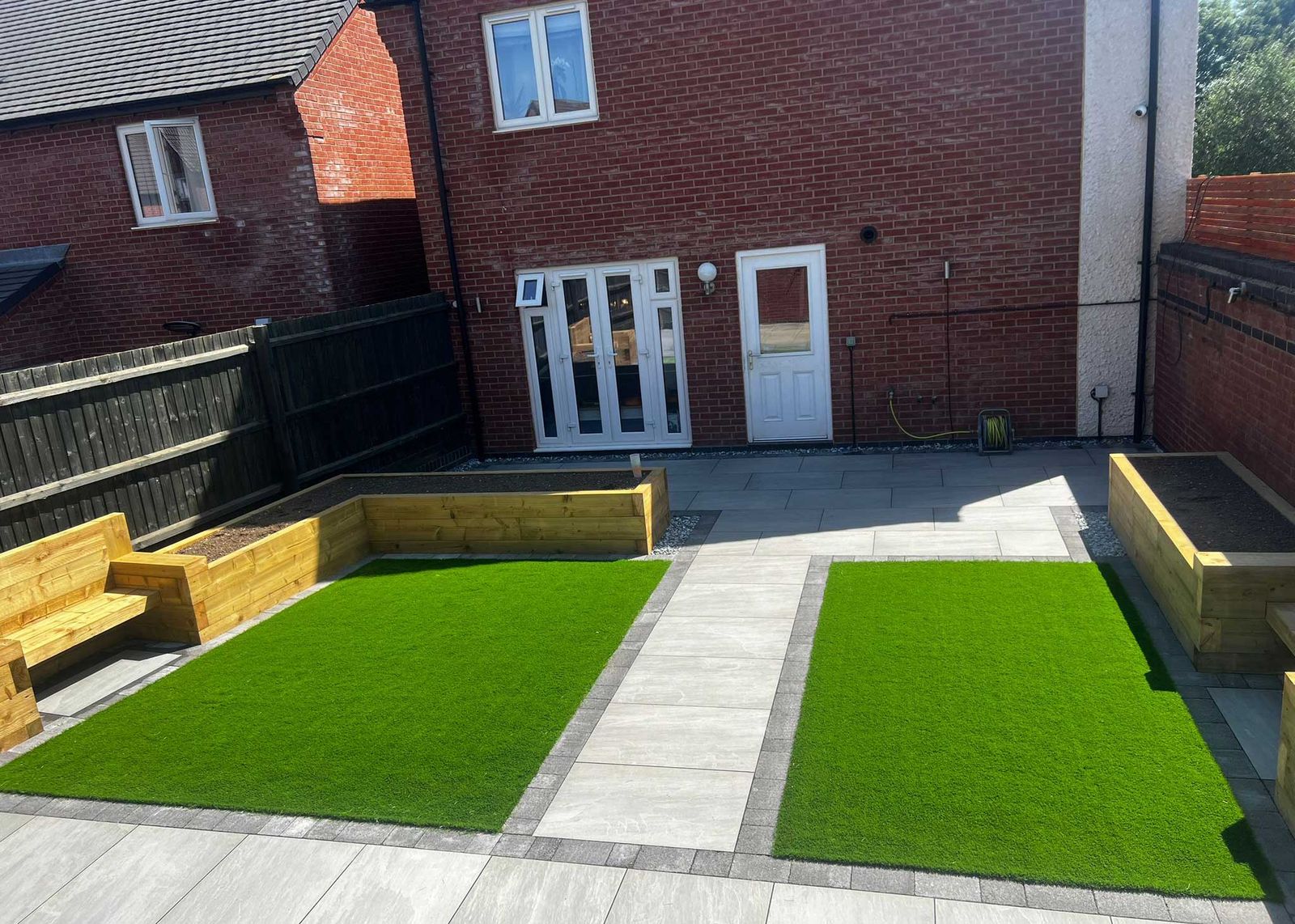 New-build garden with artificial lawns, sleeper planters and porcelain paths